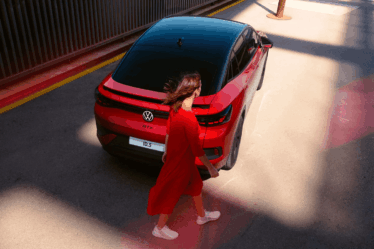 donna-in-rosso-cammina-dietro-auto-volkswagen-rossa-e-nera
