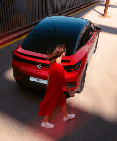donna-in-rosso-cammina-dietro-auto-volkswagen-rossa-e-nera