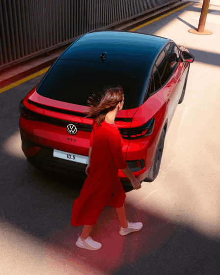 donna-in-rosso-cammina-dietro-auto-volkswagen-rossa-e-nera